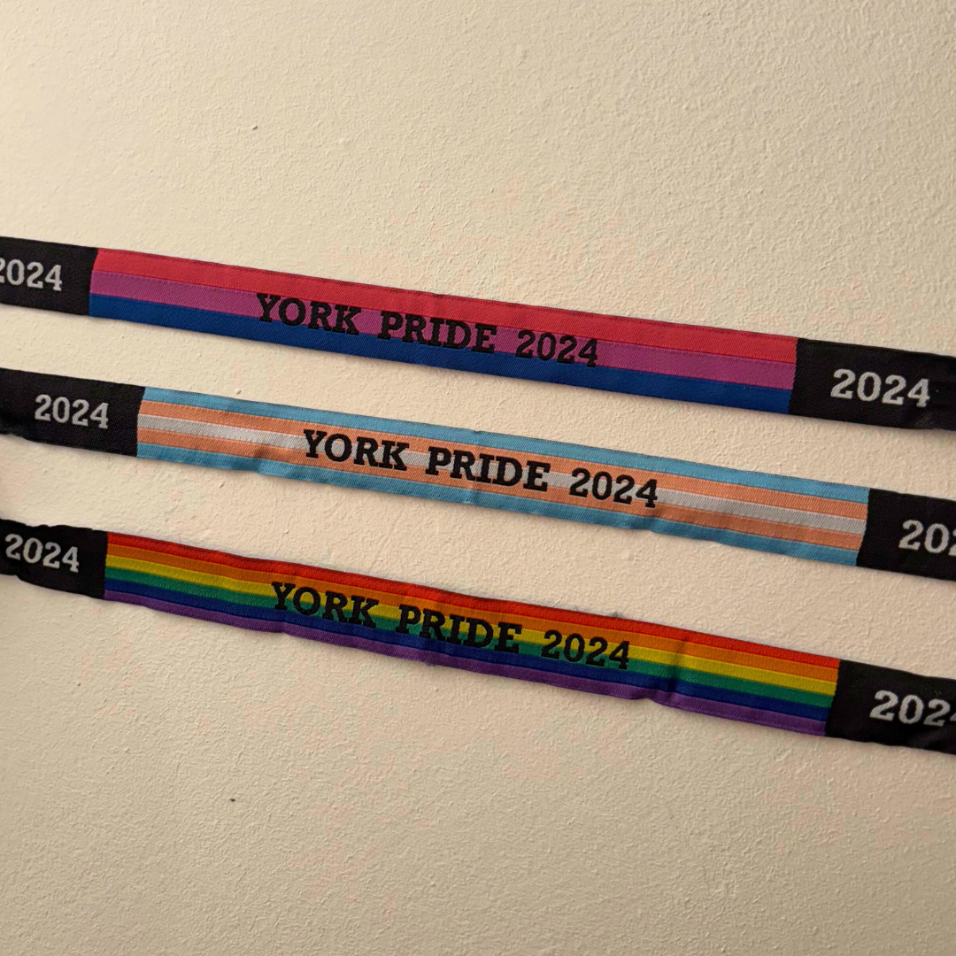 York Pride 2024 wristbands in bi, trans, and rainbow flags displayed on a wall.