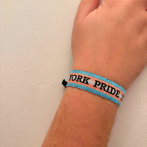 Hand wearing a York Pride 2023 wristband with pink and blue colours, against a plain background.
