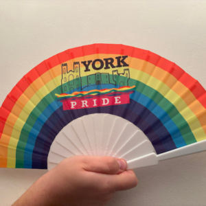 Rainbow fan with York Pride logo held by a hand, symbolising LGBT+ inclusivity and celebration.