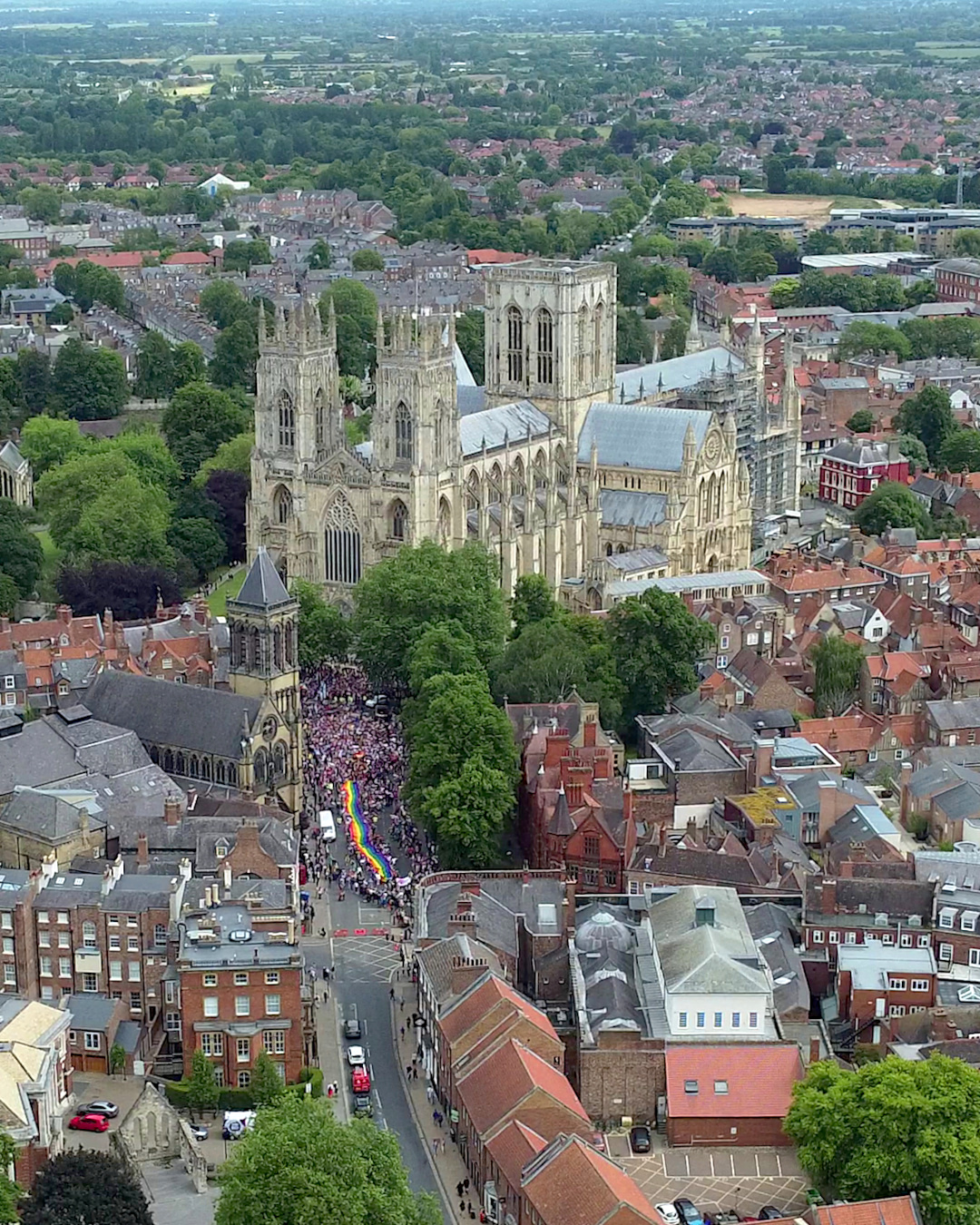 Aerial view of York Pride parade with rainbow flag near York Minster, showcasing diverse and inclusive celebration.